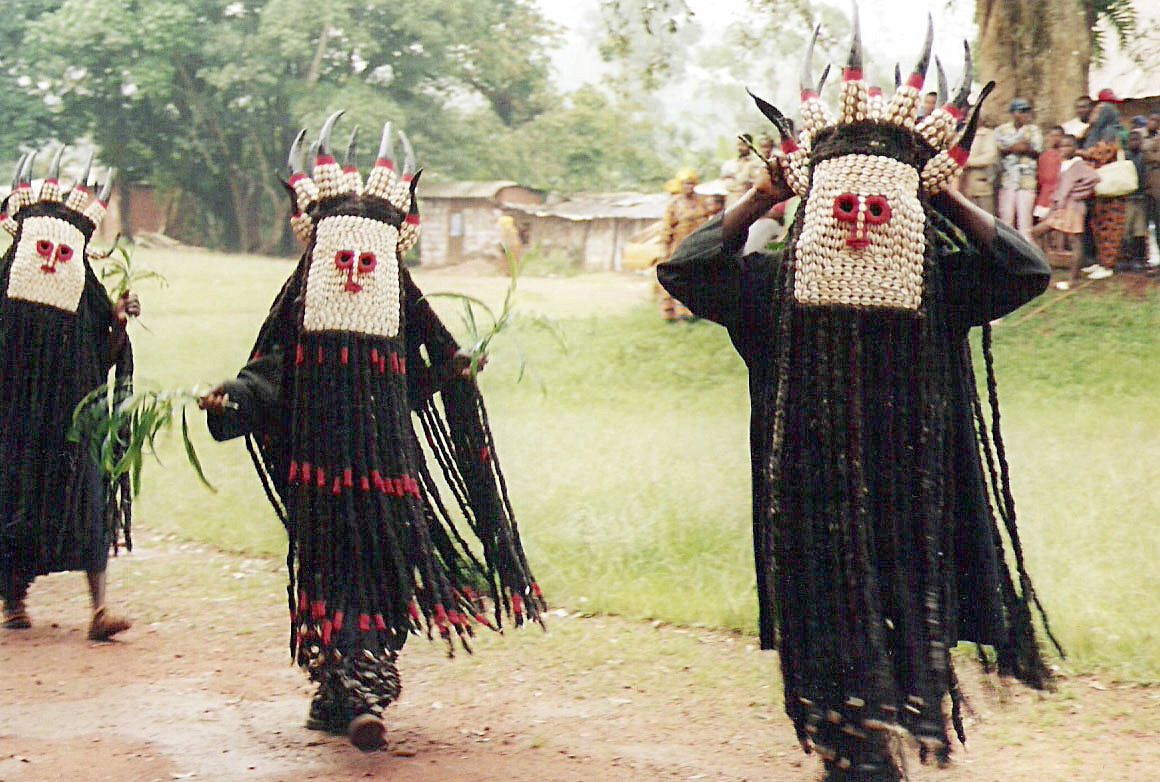 Masked dancers in cowrie headdresses performing a traditional ceremony